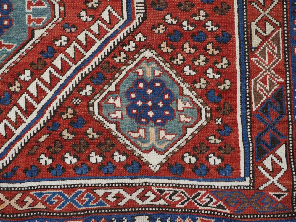 An antique hand-knotted Caucasian Shirvan Baku Khila wool rug featuring geometric diamond medallions on a red ground with navy blue and ivory borders. View XIII