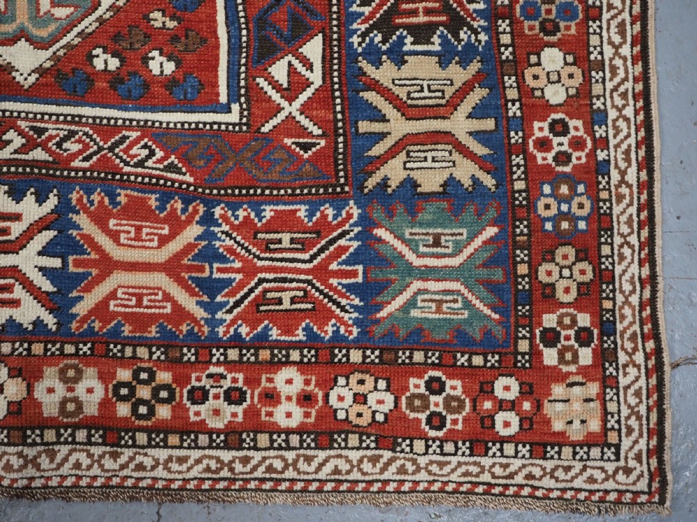 An antique hand-knotted Caucasian Shirvan Baku Khila wool rug featuring geometric diamond medallions on a red ground with navy blue and ivory borders. View XIV