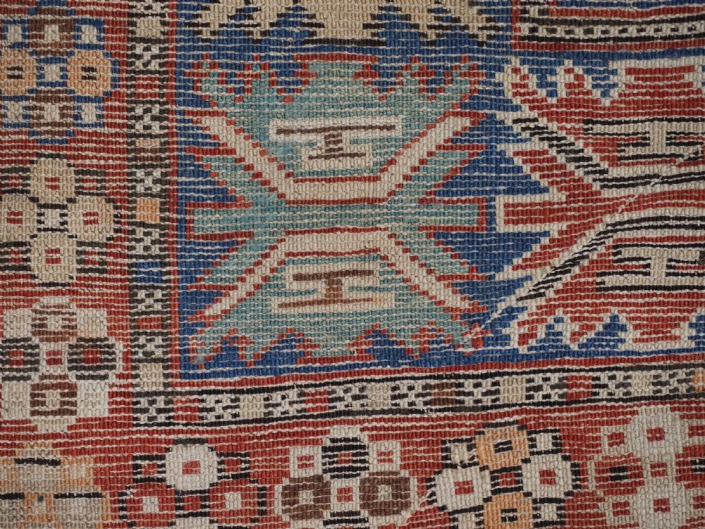An antique hand-knotted Caucasian Shirvan Baku Khila wool rug featuring geometric diamond medallions on a red ground with navy blue and ivory borders. View XV