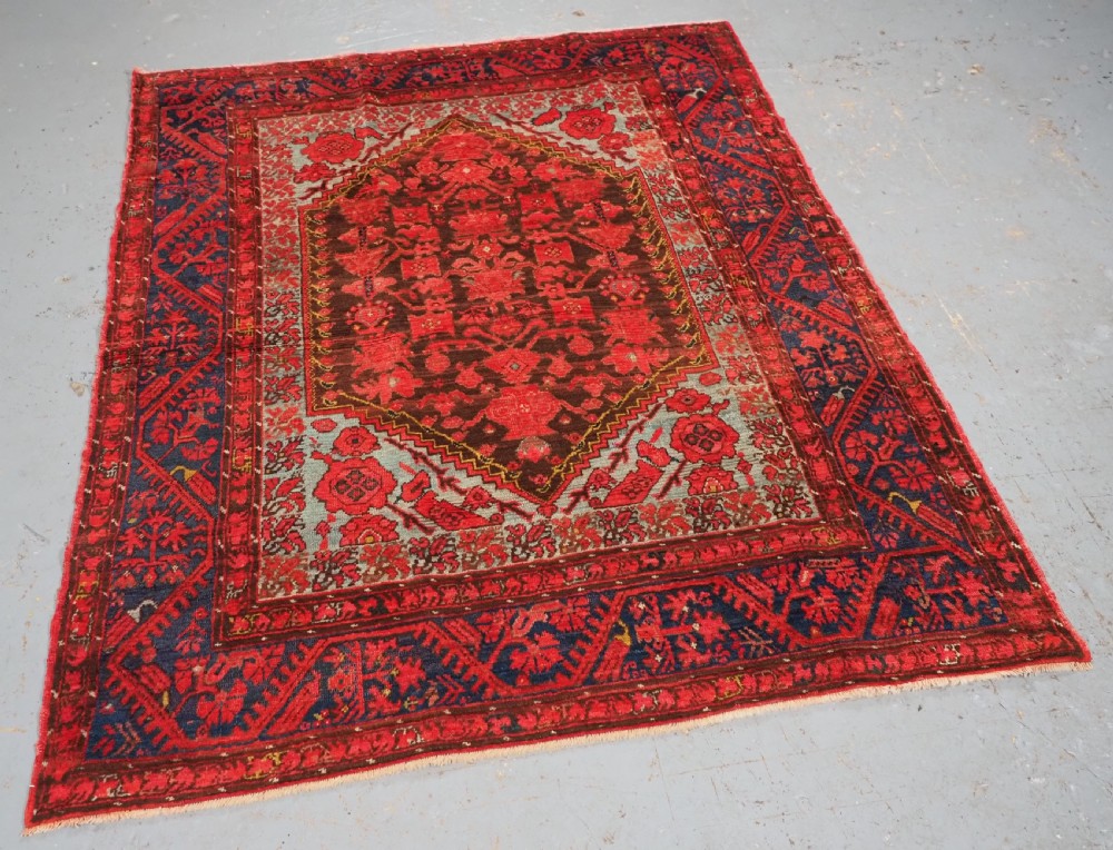 An antique hand-knotted Turkish Komurcu Kula wool rug featuring a central diamond medallion in crimson red, deep blue, dark brown, and grey-blue tones. View II