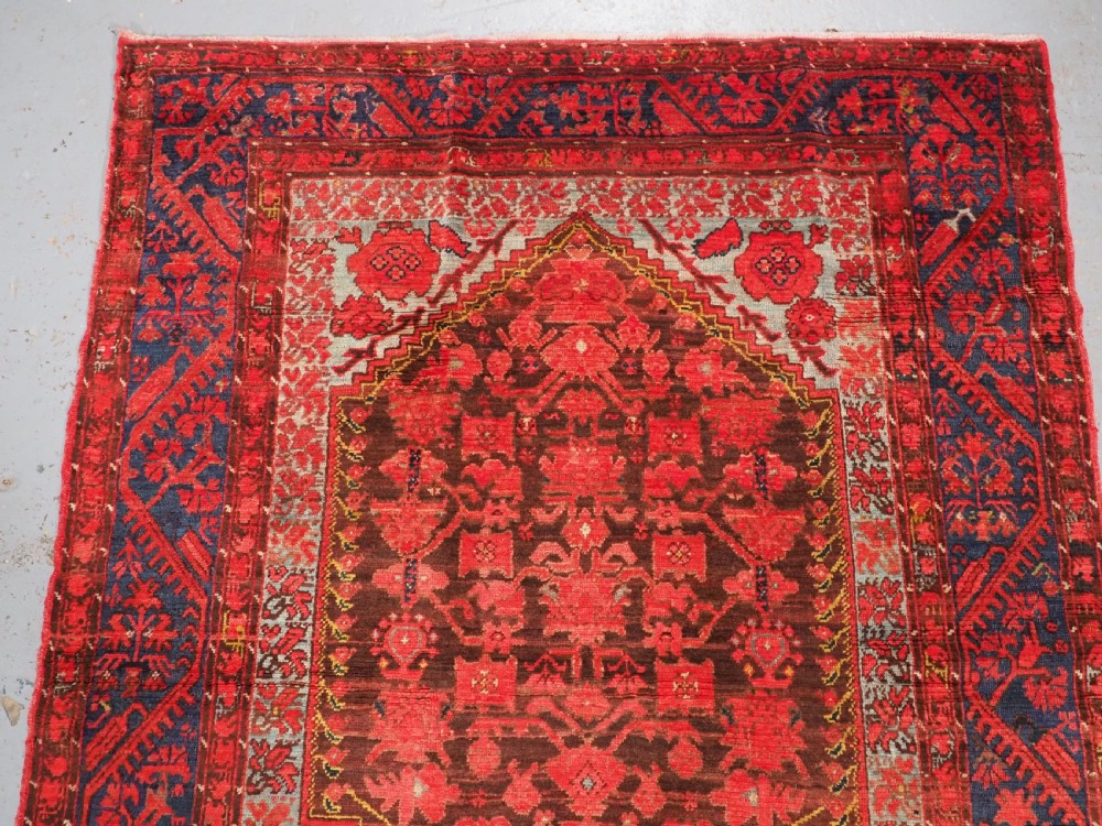 An antique hand-knotted Turkish Komurcu Kula wool rug featuring a central diamond medallion in crimson red, deep blue, dark brown, and grey-blue tones. View III