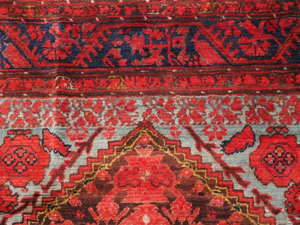 An antique hand-knotted Turkish Komurcu Kula wool rug featuring a central diamond medallion in crimson red, deep blue, dark brown, and grey-blue tones. View VIII