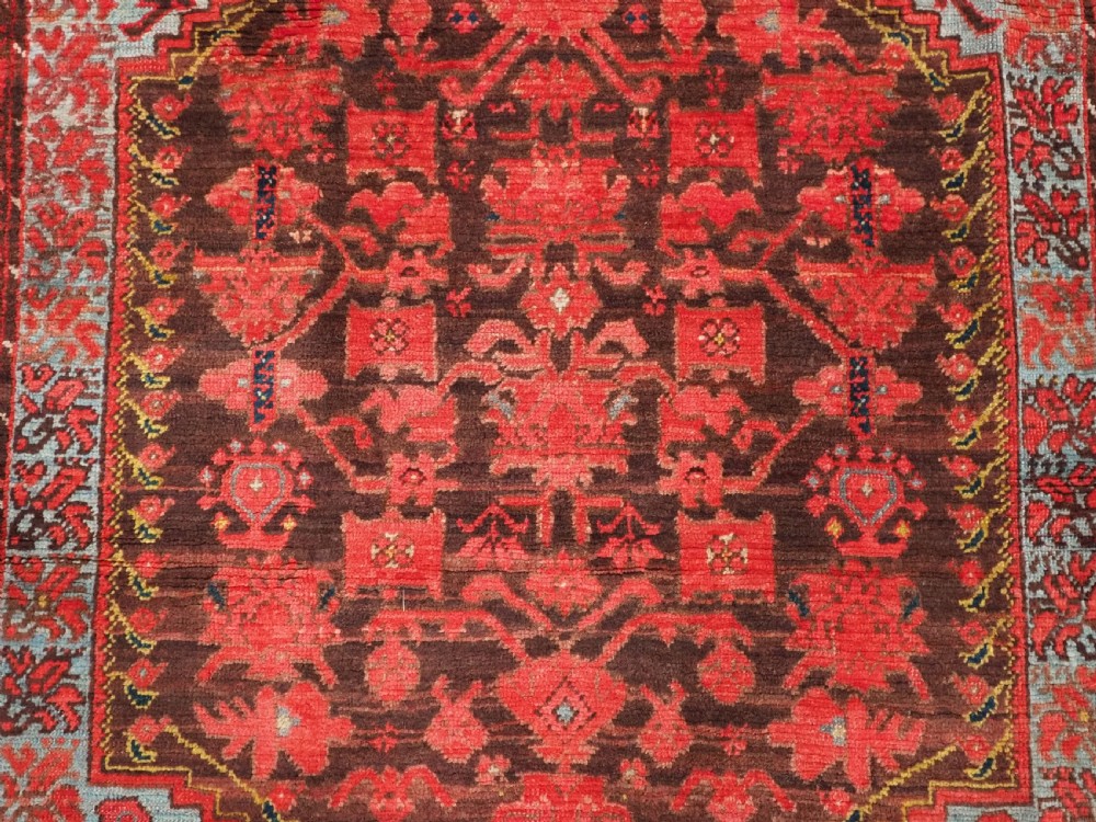 An antique hand-knotted Turkish Komurcu Kula wool rug featuring a central diamond medallion in crimson red, deep blue, dark brown, and grey-blue tones. View IX