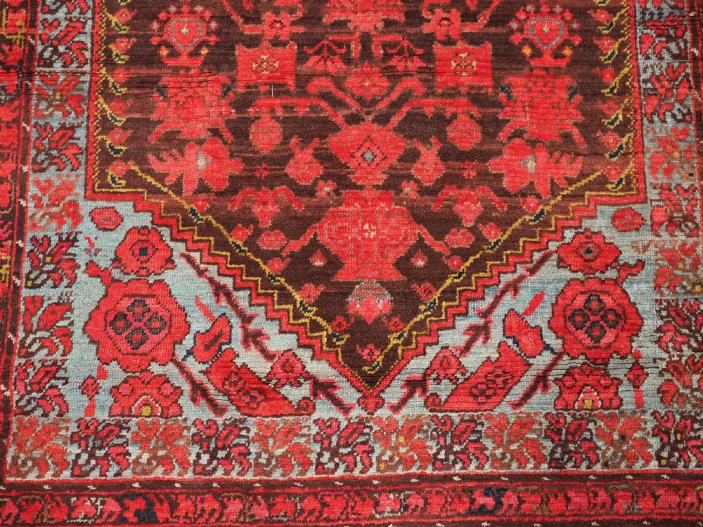 An antique hand-knotted Turkish Komurcu Kula wool rug featuring a central diamond medallion in crimson red, deep blue, dark brown, and grey-blue tones. View X