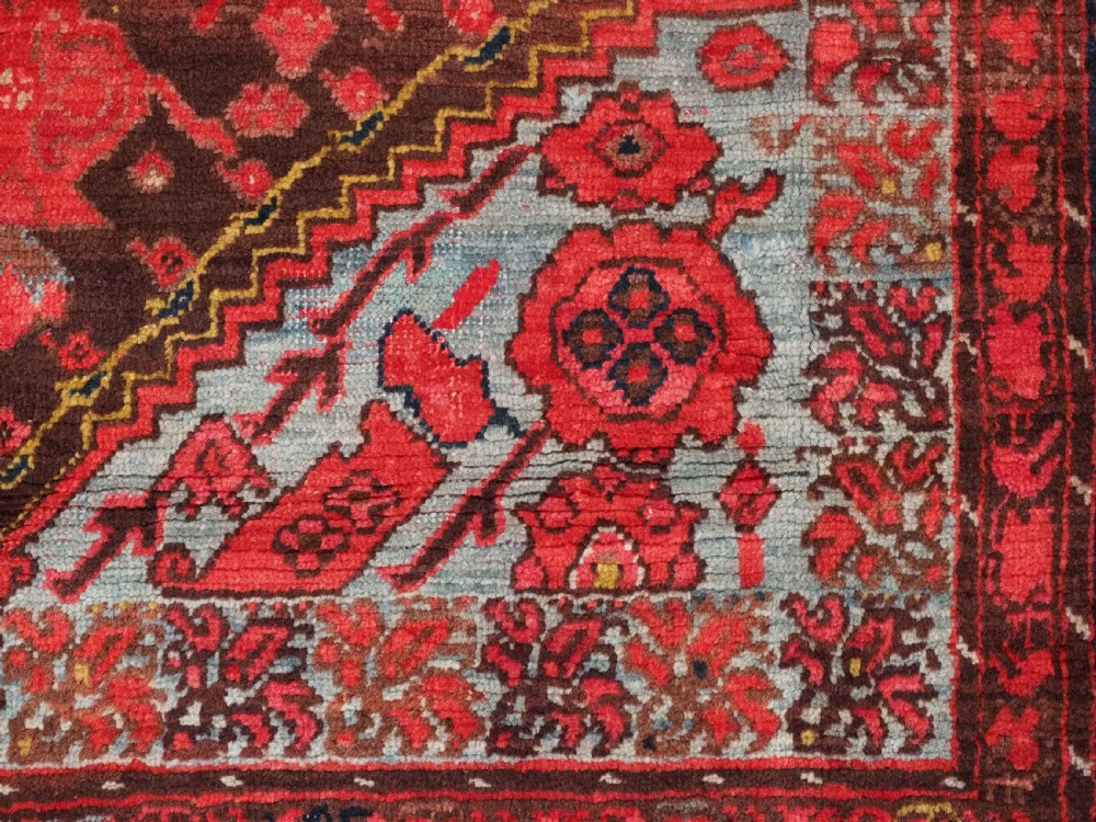 An antique hand-knotted Turkish Komurcu Kula wool rug featuring a central diamond medallion in crimson red, deep blue, dark brown, and grey-blue tones. View XI