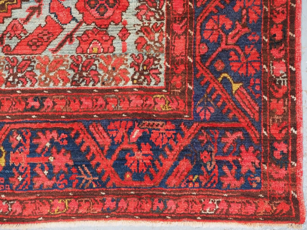 An antique hand-knotted Turkish Komurcu Kula wool rug featuring a central diamond medallion in crimson red, deep blue, dark brown, and grey-blue tones. View XII