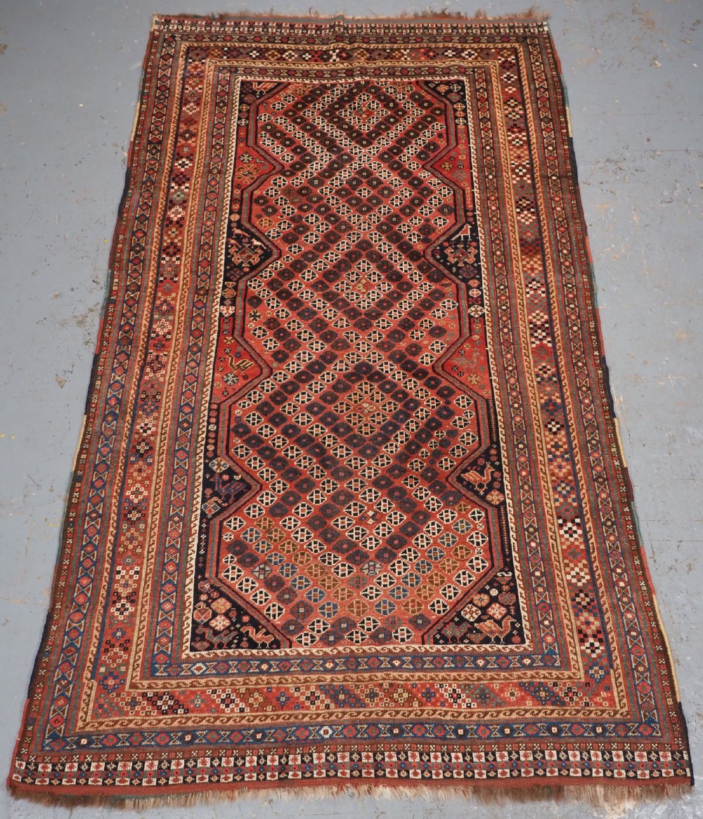 An antique Qashqai hand-knotted wool rug featuring a red and navy diamond lattice pattern with multi-band geometric borders.