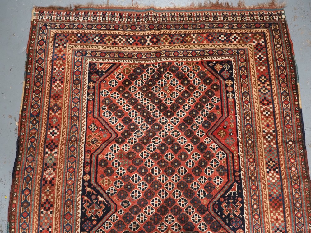 An antique Qashqai hand-knotted wool rug featuring a red and navy diamond lattice pattern with multi-band geometric borders. View III