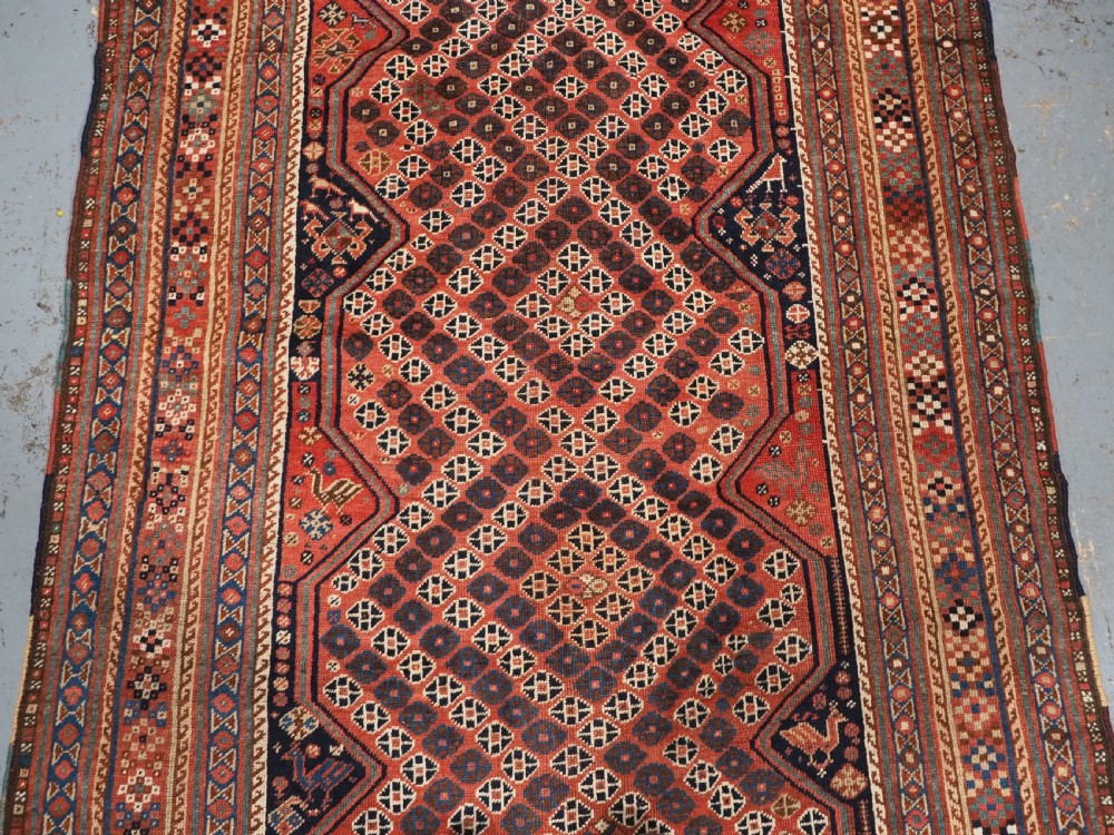 An antique Qashqai hand-knotted wool rug featuring a red and navy diamond lattice pattern with multi-band geometric borders. View IV
