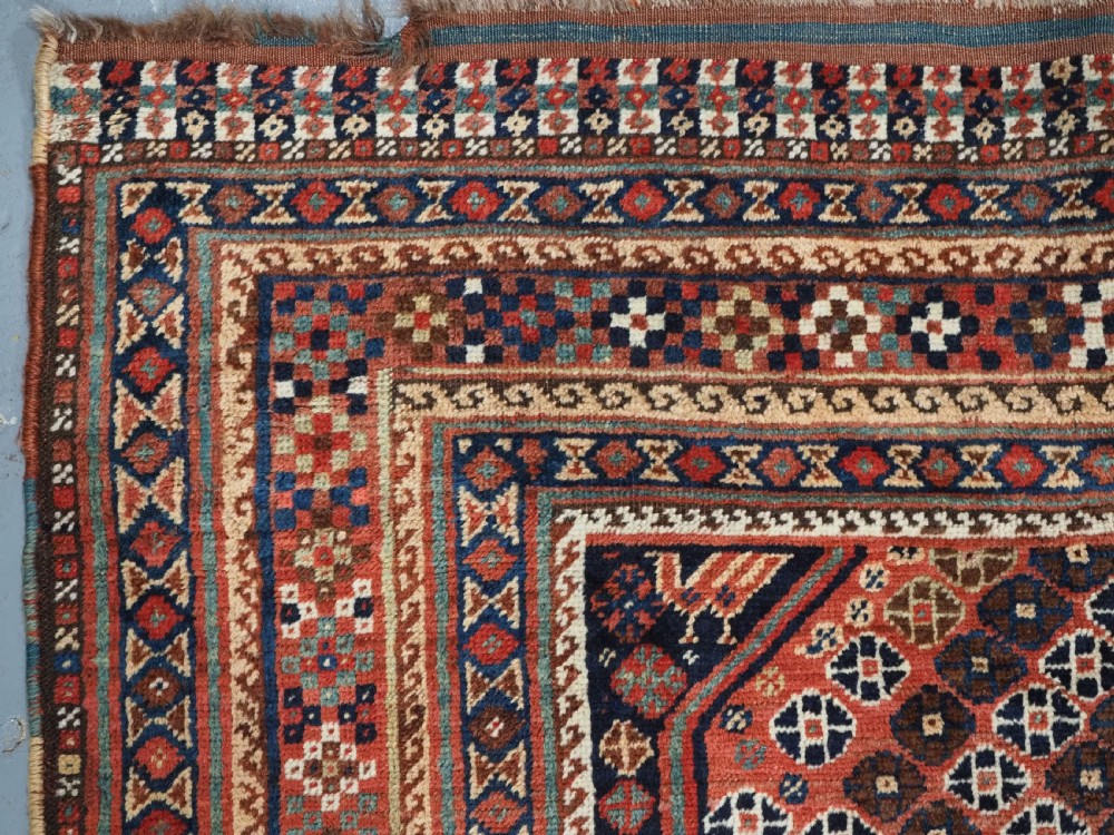 An antique Qashqai hand-knotted wool rug featuring a red and navy diamond lattice pattern with multi-band geometric borders. View V
