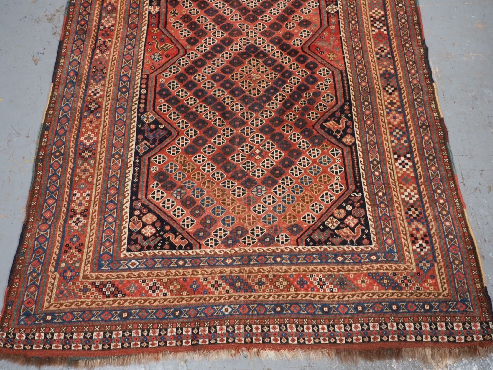 An antique Qashqai hand-knotted wool rug featuring a red and navy diamond lattice pattern with multi-band geometric borders. View VI