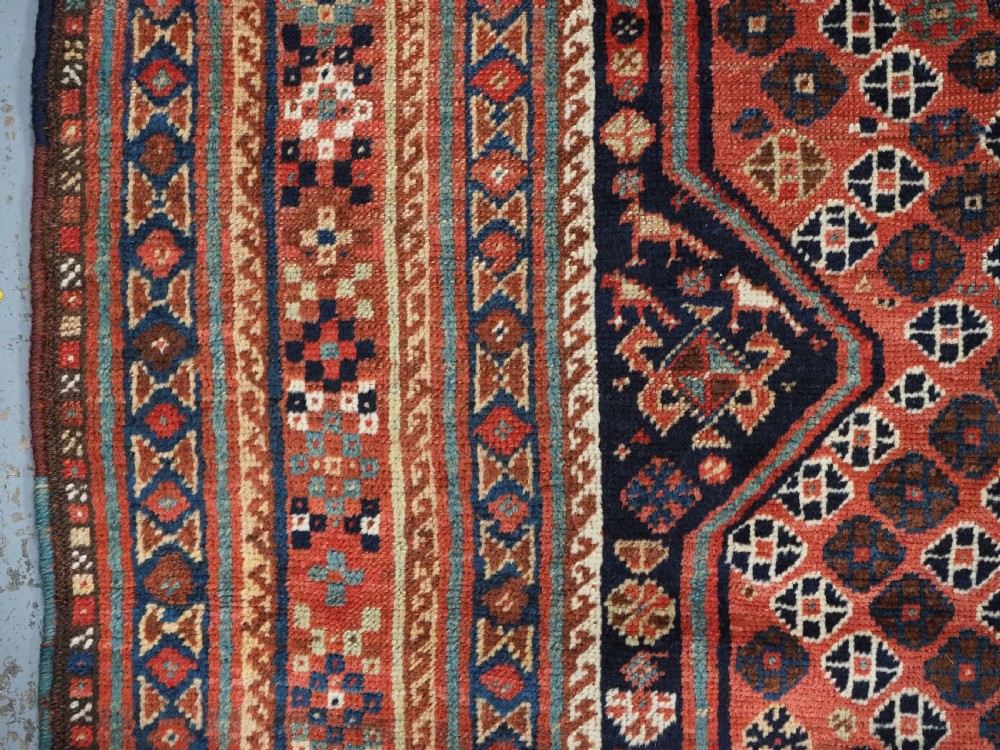 An antique Qashqai hand-knotted wool rug featuring a red and navy diamond lattice pattern with multi-band geometric borders. View VII
