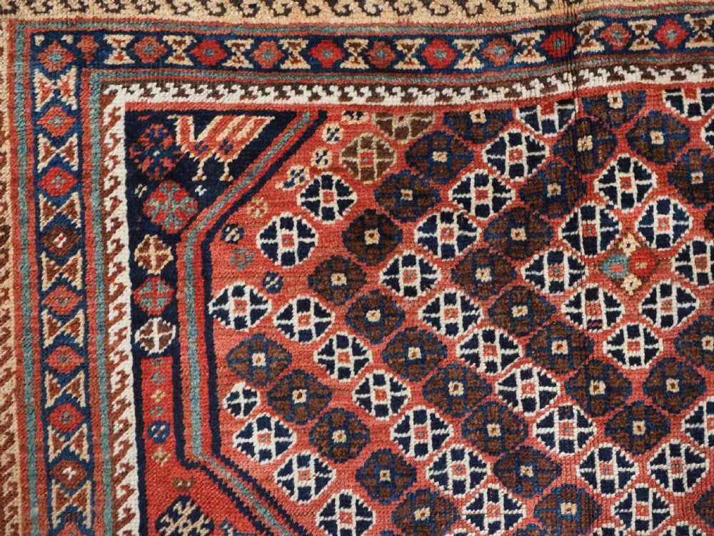 An antique Qashqai hand-knotted wool rug featuring a red and navy diamond lattice pattern with multi-band geometric borders. View VIII
