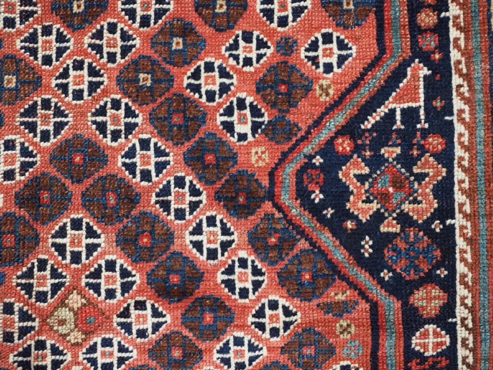 An antique Qashqai hand-knotted wool rug featuring a red and navy diamond lattice pattern with multi-band geometric borders. View X