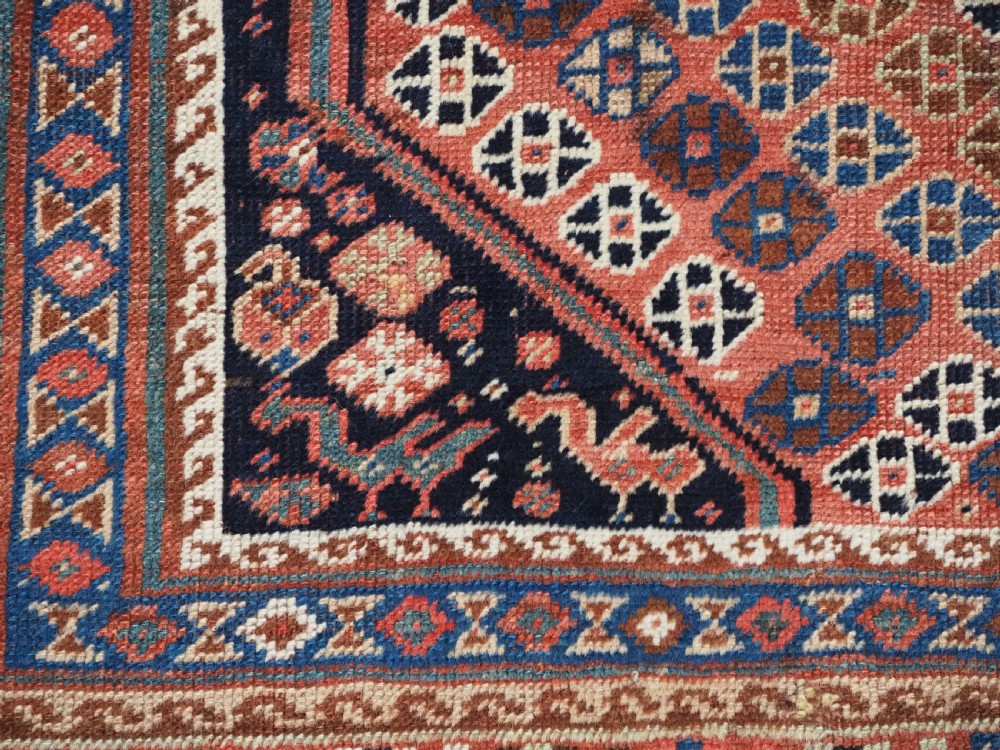 An antique Qashqai hand-knotted wool rug featuring a red and navy diamond lattice pattern with multi-band geometric borders. View XV