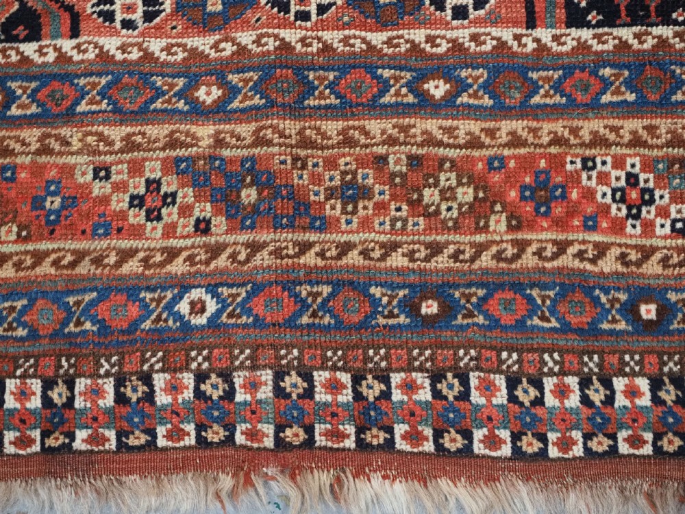 An antique Qashqai hand-knotted wool rug featuring a red and navy diamond lattice pattern with multi-band geometric borders. View XVI