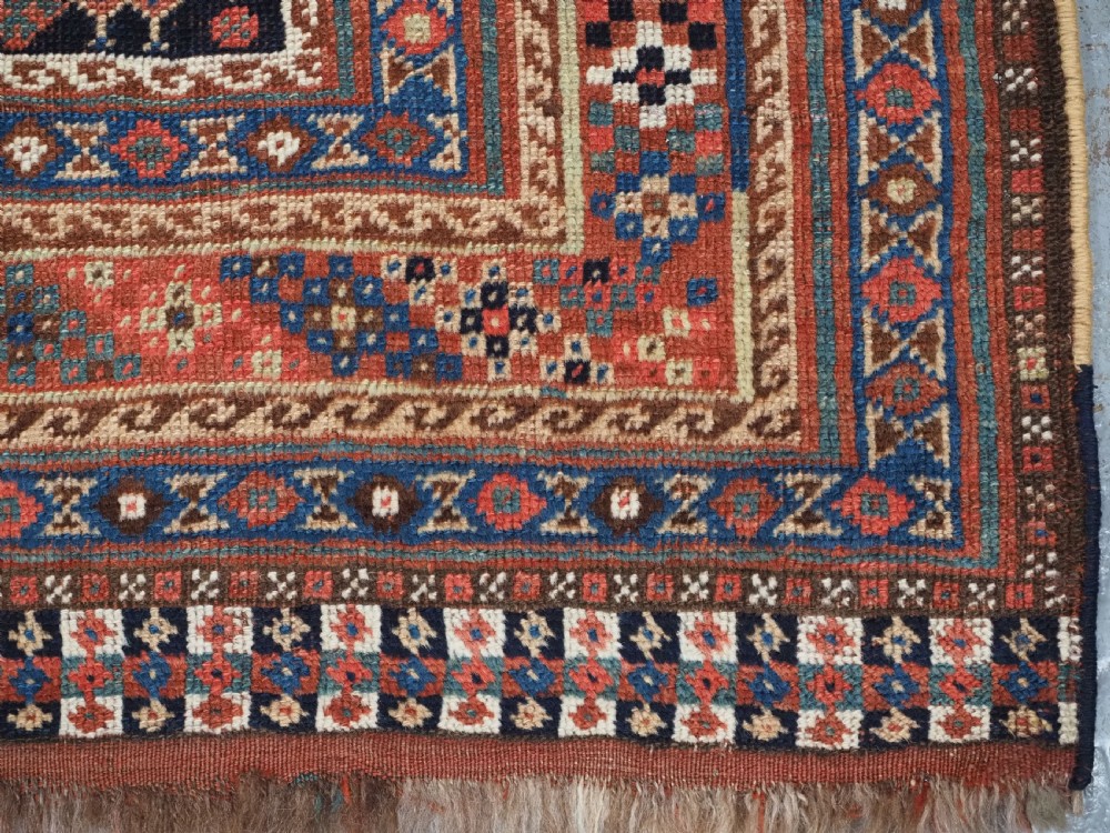 An antique Qashqai hand-knotted wool rug featuring a red and navy diamond lattice pattern with multi-band geometric borders. View XVII