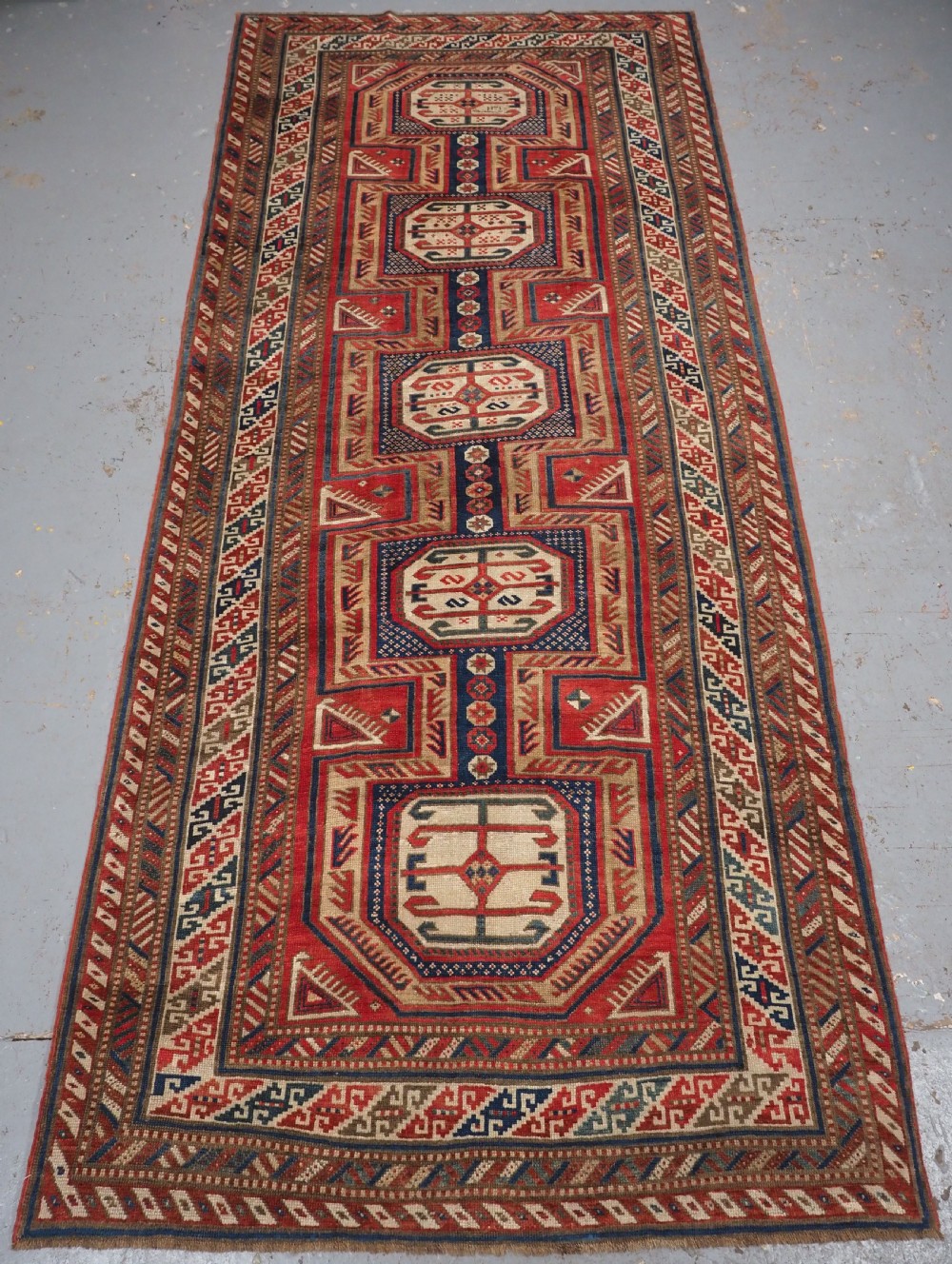An antique Caucasian Shirvan long wool runner rug featuring terracotta red, navy blue, and beige octagonal geometric medallions within patterned borders.