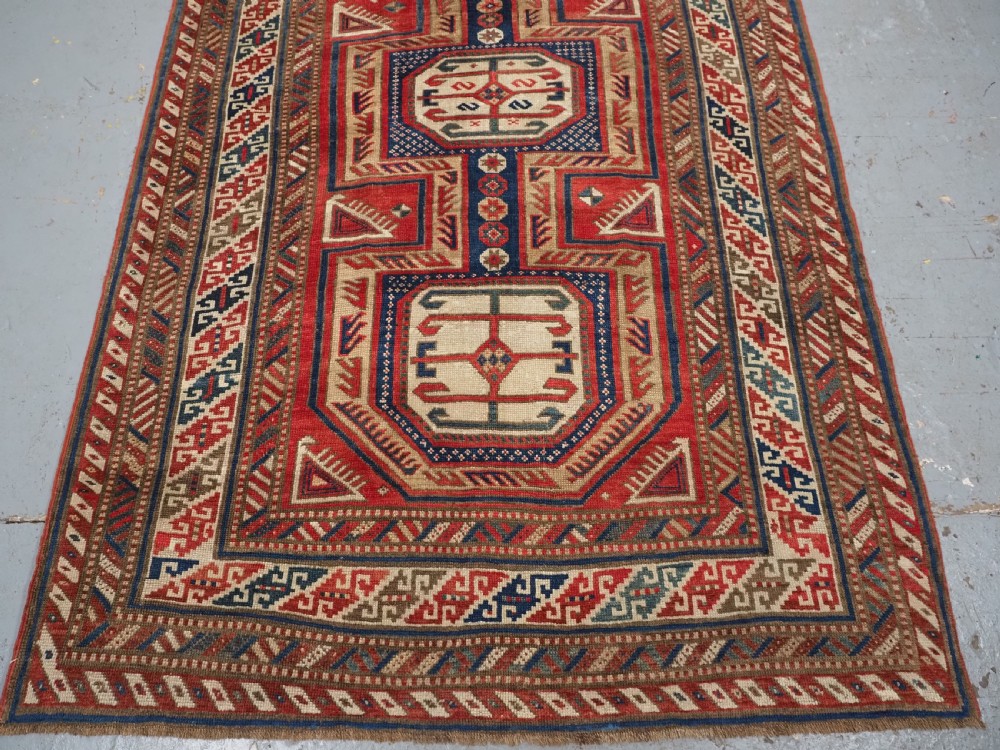 An antique Caucasian Shirvan long wool runner rug featuring terracotta red, navy blue, and beige octagonal geometric medallions within patterned borders. View V