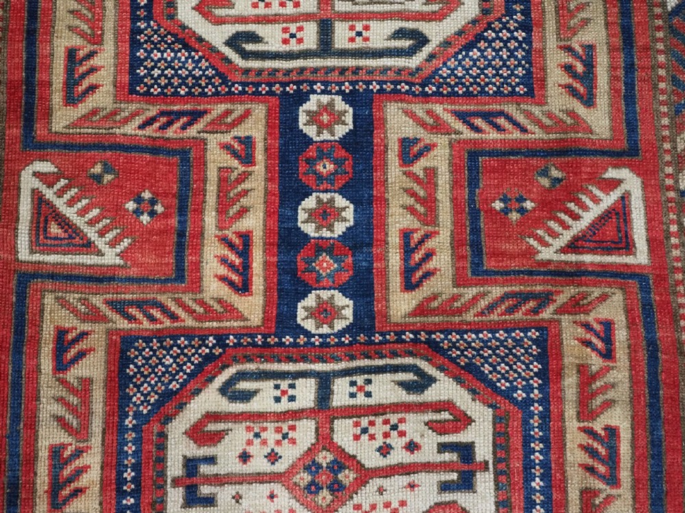 An antique Caucasian Shirvan long wool runner rug featuring terracotta red, navy blue, and beige octagonal geometric medallions within patterned borders. View X