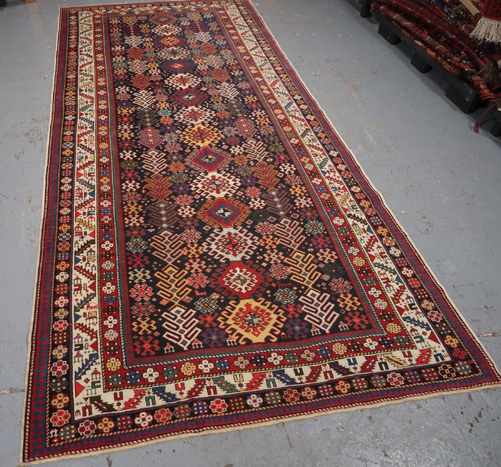 An antique long Caucasian runner rug featuring a dark navy field filled with multi-coloured hooked diamond medallions and detailed geometric borders. View II
