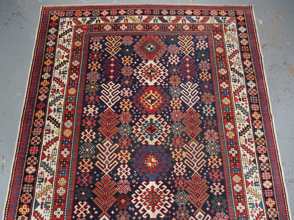 An antique long Caucasian runner rug featuring a dark navy field filled with multi-coloured hooked diamond medallions and detailed geometric borders. View III