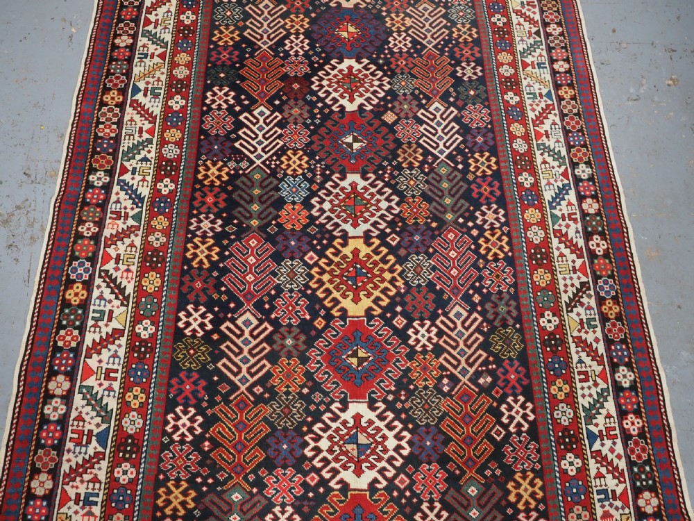 An antique long Caucasian runner rug featuring a dark navy field filled with multi-coloured hooked diamond medallions and detailed geometric borders. View IV
