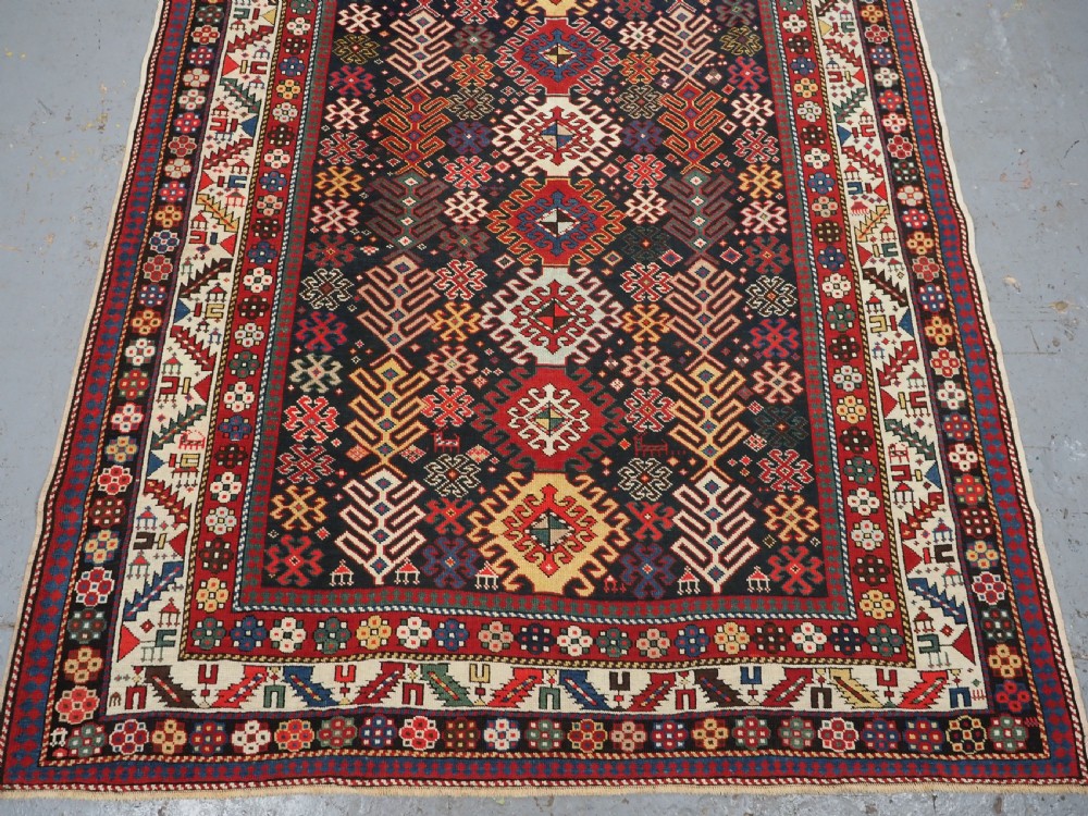 An antique long Caucasian runner rug featuring a dark navy field filled with multi-coloured hooked diamond medallions and detailed geometric borders. View V