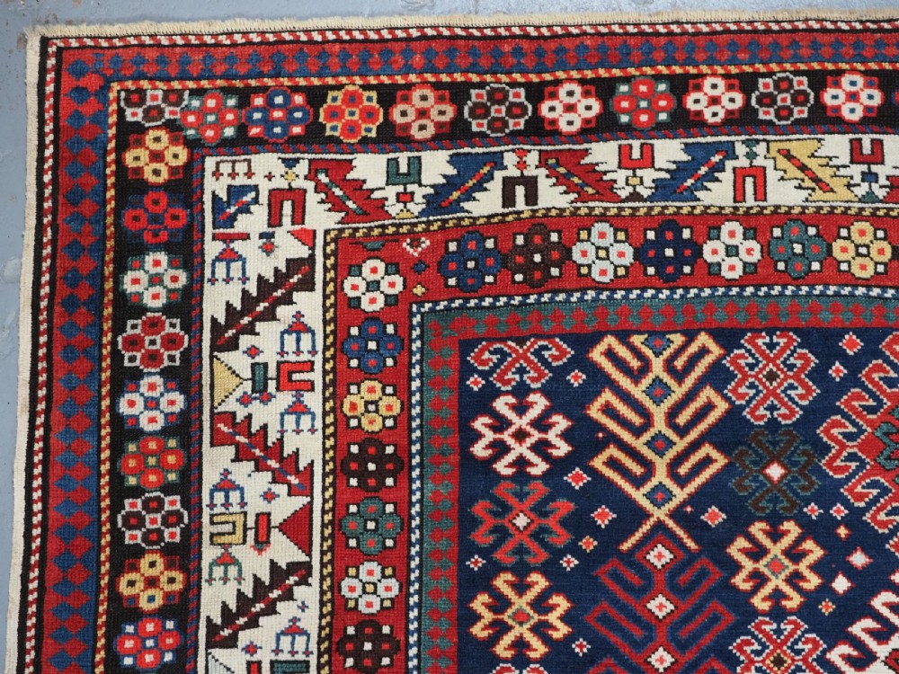 An antique long Caucasian runner rug featuring a dark navy field filled with multi-coloured hooked diamond medallions and detailed geometric borders. View VI