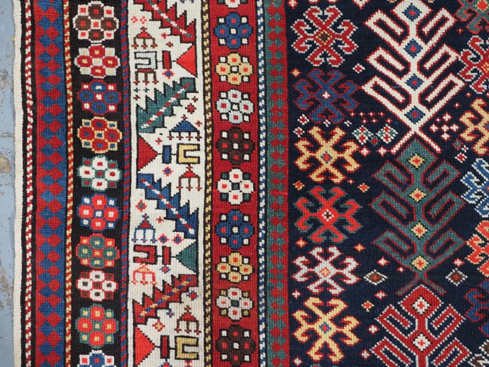 An antique long Caucasian runner rug featuring a dark navy field filled with multi-coloured hooked diamond medallions and detailed geometric borders. View VII
