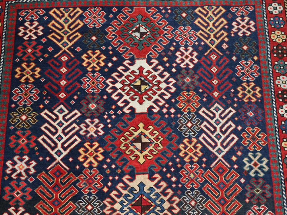 An antique long Caucasian runner rug featuring a dark navy field filled with multi-coloured hooked diamond medallions and detailed geometric borders. View VIII