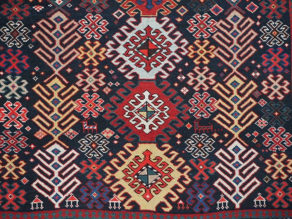 An antique long Caucasian runner rug featuring a dark navy field filled with multi-coloured hooked diamond medallions and detailed geometric borders. View XI
