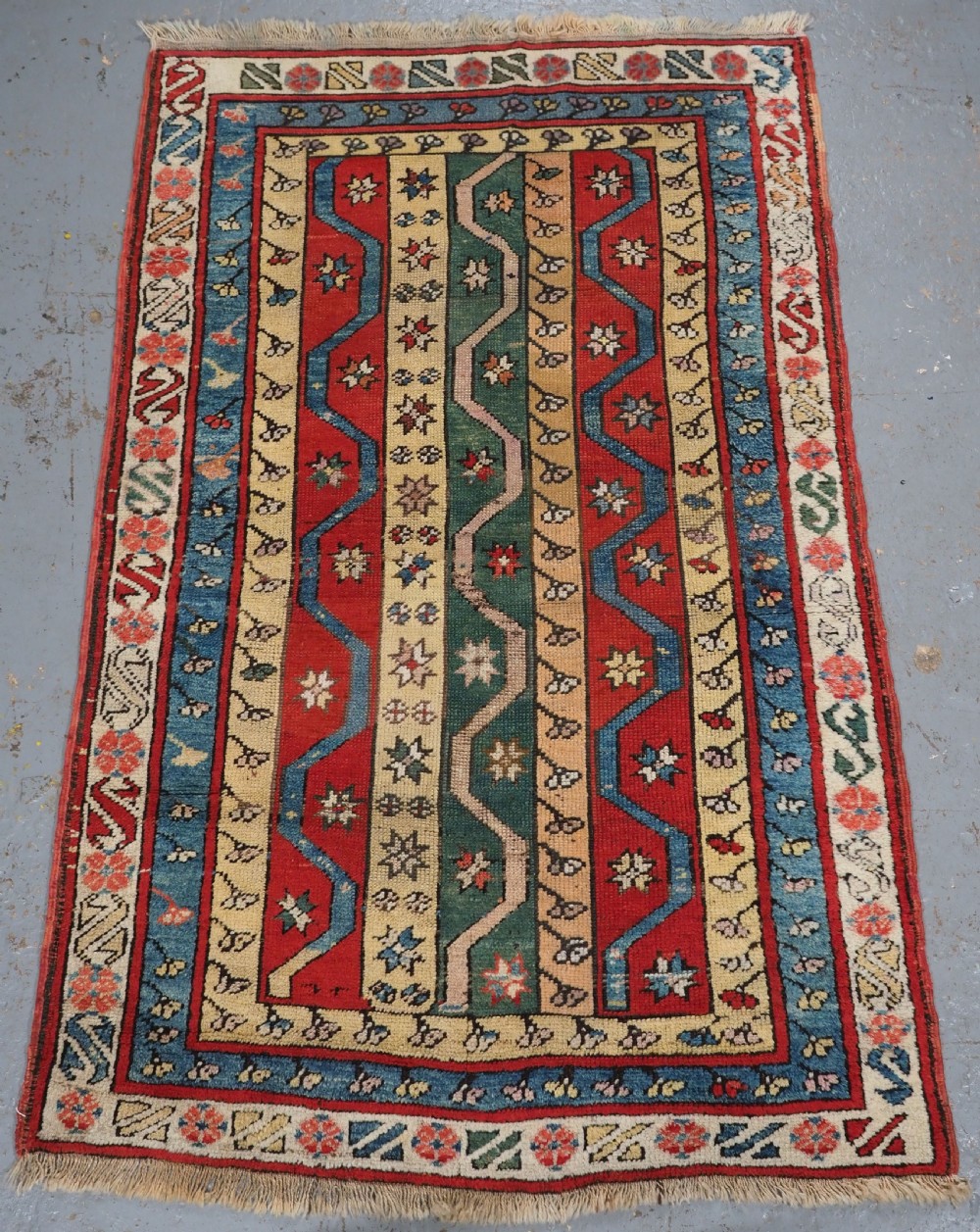 An antique hand-knotted Turkish Konya region wool rug featuring vertical geometric bands in red, blue, green, and cream with star and zig-zag motifs.