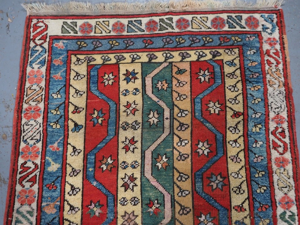 An antique hand-knotted Turkish Konya region wool rug featuring vertical geometric bands in red, blue, green, and cream with star and zig-zag motifs. View III