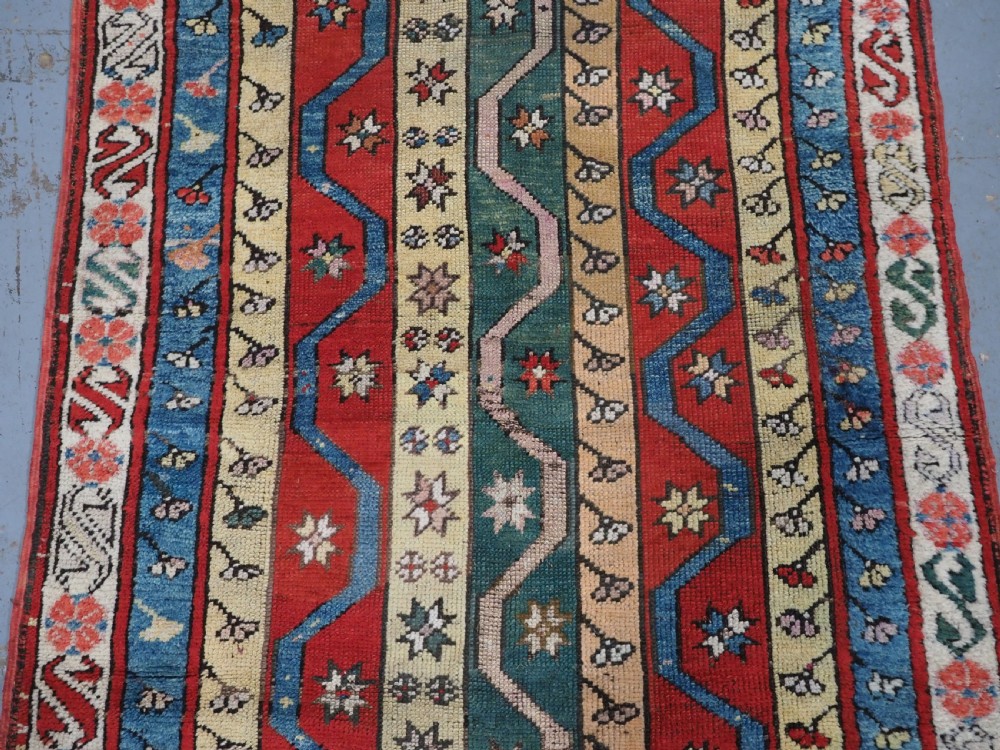 An antique hand-knotted Turkish Konya region wool rug featuring vertical geometric bands in red, blue, green, and cream with star and zig-zag motifs. View IV