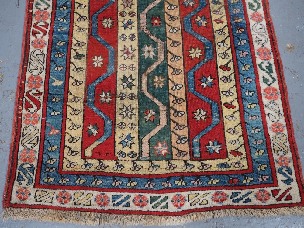 An antique hand-knotted Turkish Konya region wool rug featuring vertical geometric bands in red, blue, green, and cream with star and zig-zag motifs. View V