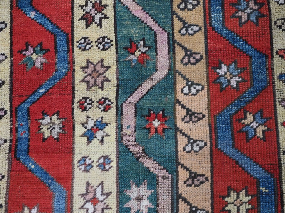 An antique hand-knotted Turkish Konya region wool rug featuring vertical geometric bands in red, blue, green, and cream with star and zig-zag motifs. View IX