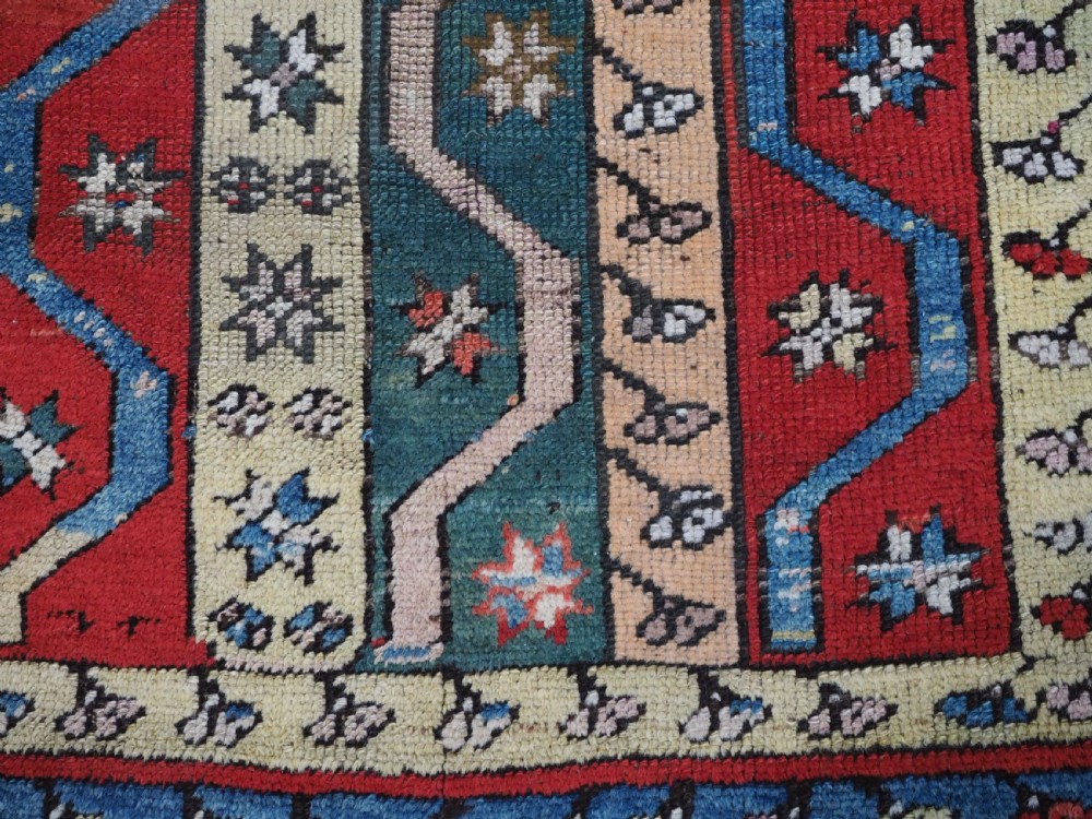 An antique hand-knotted Turkish Konya region wool rug featuring vertical geometric bands in red, blue, green, and cream with star and zig-zag motifs. View X