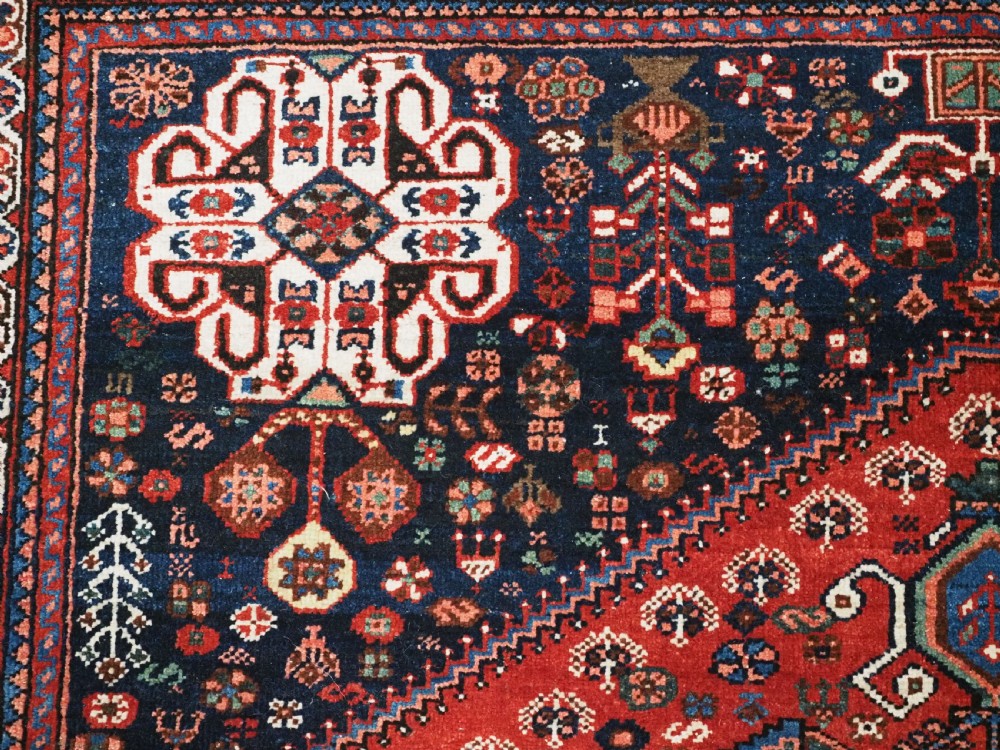 An antique hand-knotted Abadeh wool rug featuring a central diamond medallion, terracotta red field, and navy blue borders with intricate tribal geometric patterns. View VIII