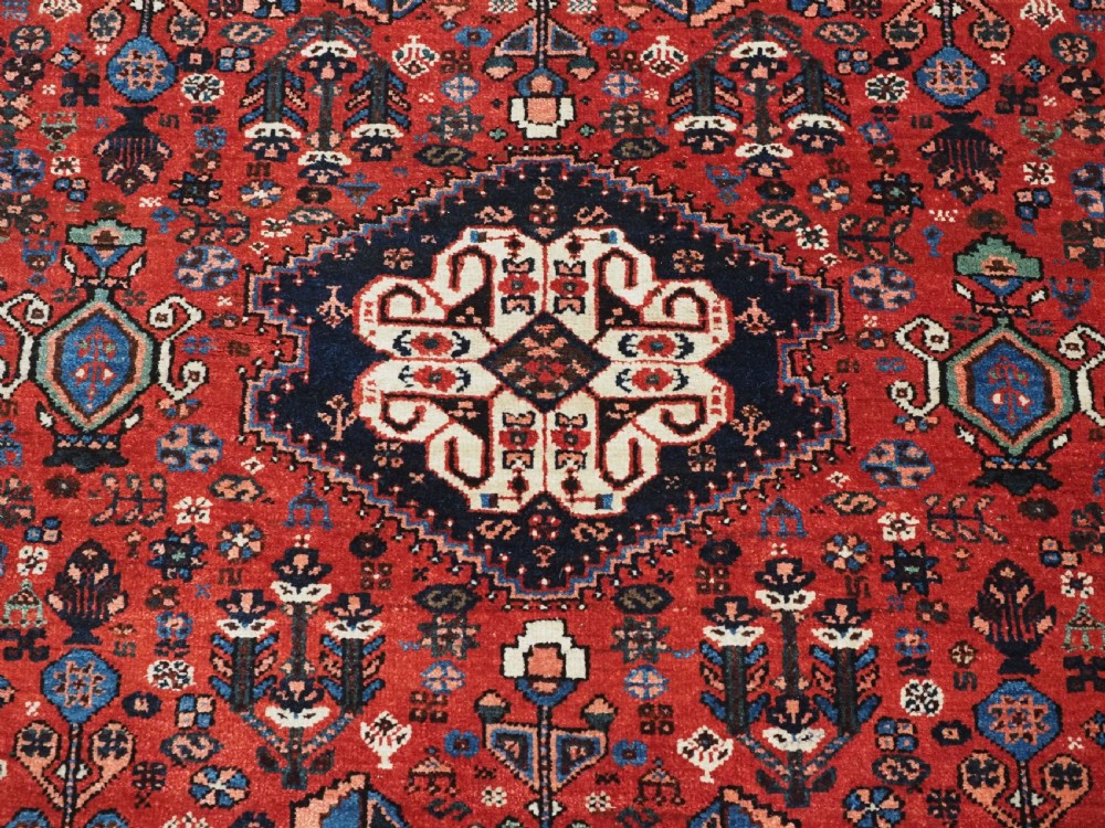 An antique hand-knotted Abadeh wool rug featuring a central diamond medallion, terracotta red field, and navy blue borders with intricate tribal geometric patterns. View XI