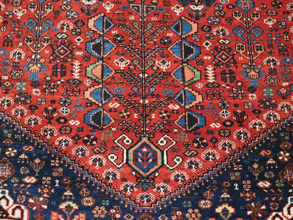 An antique hand-knotted Abadeh wool rug featuring a central diamond medallion, terracotta red field, and navy blue borders with intricate tribal geometric patterns. View XII