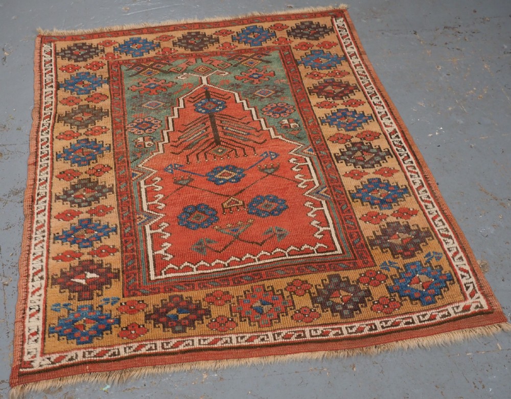 An antique hand-knotted Turkish Konya prayer rug featuring a stepped central red niche surrounded by green, blue, and ochre geometric motifs. View II