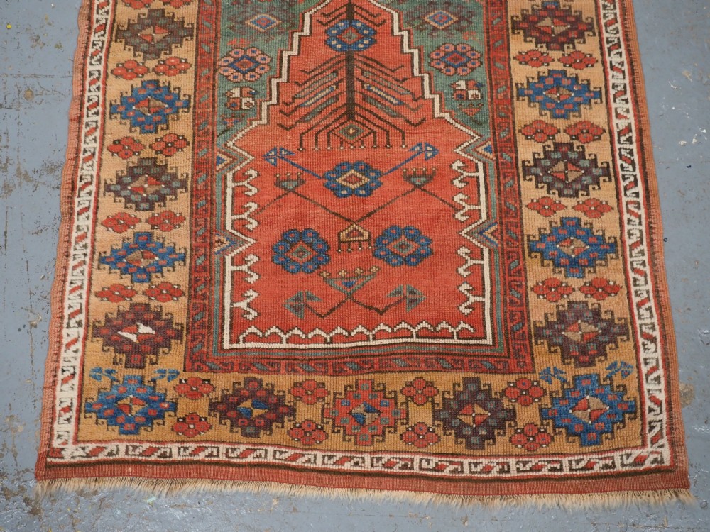 An antique hand-knotted Turkish Konya prayer rug featuring a stepped central red niche surrounded by green, blue, and ochre geometric motifs. View IV