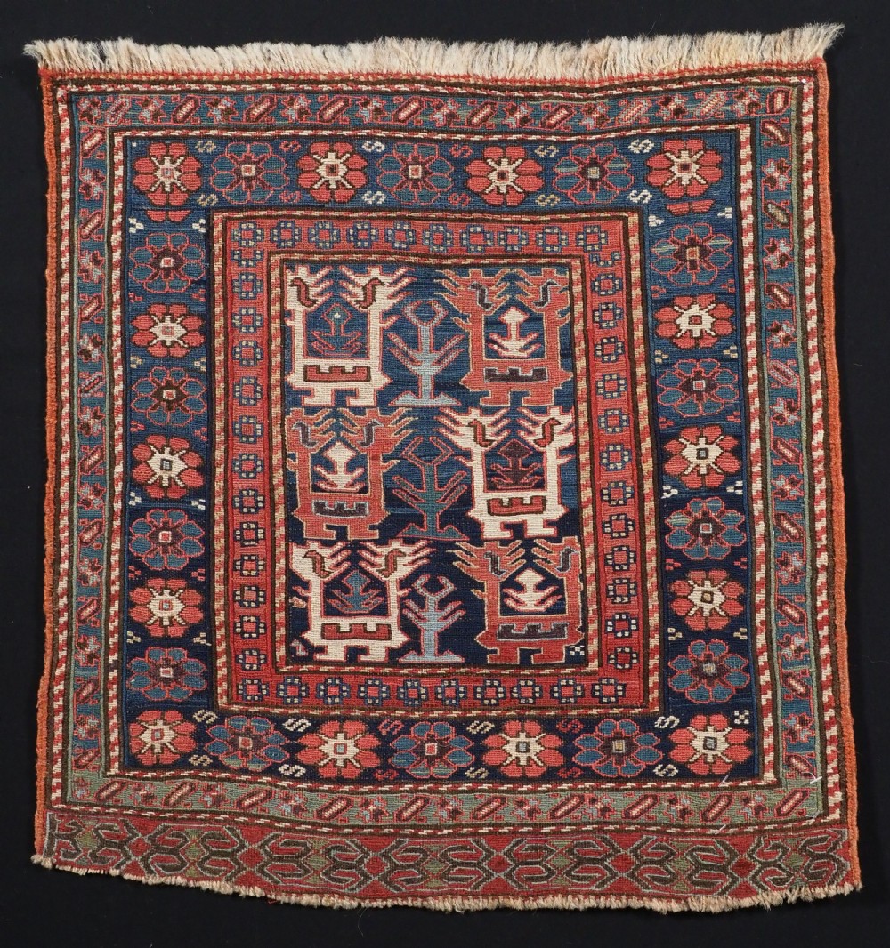 A square antique woven wool Shahsavan Soumak textile panel displaying geometric dragon and bird motifs on a dark navy background framed by red floral borders.
