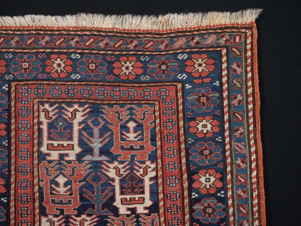 A square antique woven wool Shahsavan Soumak textile panel displaying geometric dragon and bird motifs on a dark navy background framed by red floral borders. View III