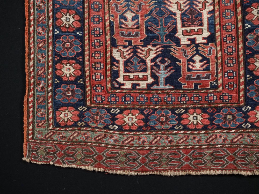 A square antique woven wool Shahsavan Soumak textile panel displaying geometric dragon and bird motifs on a dark navy background framed by red floral borders. View IV