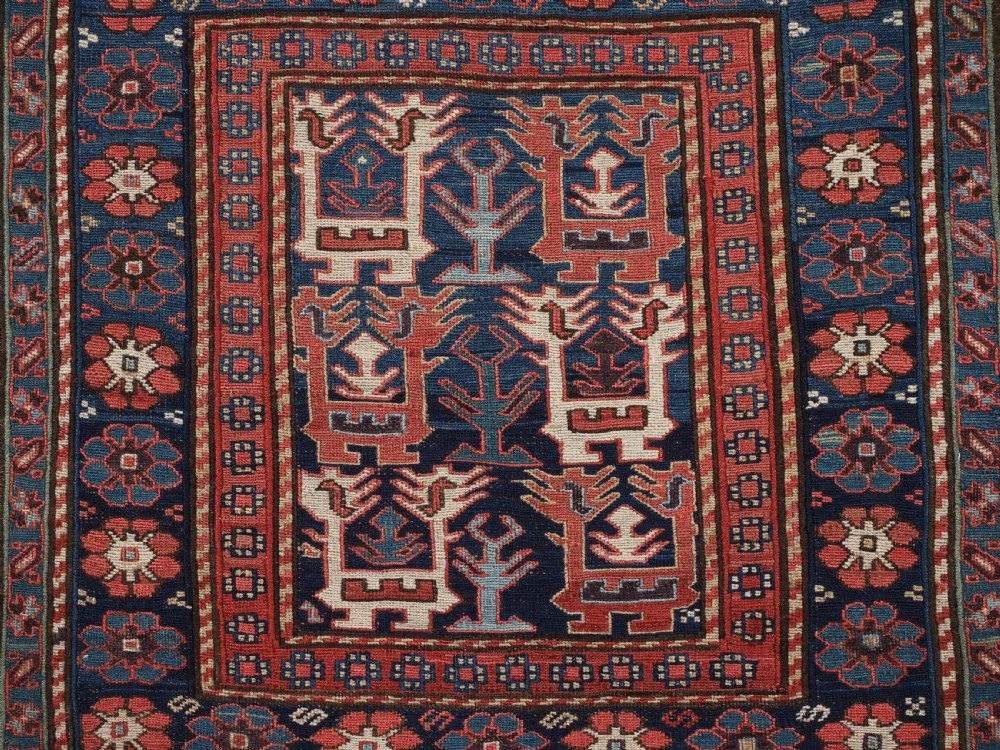 A square antique woven wool Shahsavan Soumak textile panel displaying geometric dragon and bird motifs on a dark navy background framed by red floral borders. View V
