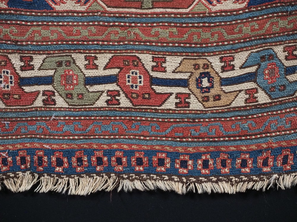 A square antique Shahsevan Soumak woven wool panel featuring central geometric octagonal medallions flanked by bird and dragon motifs in shades of terracotta red, blue, and ivory. View VII