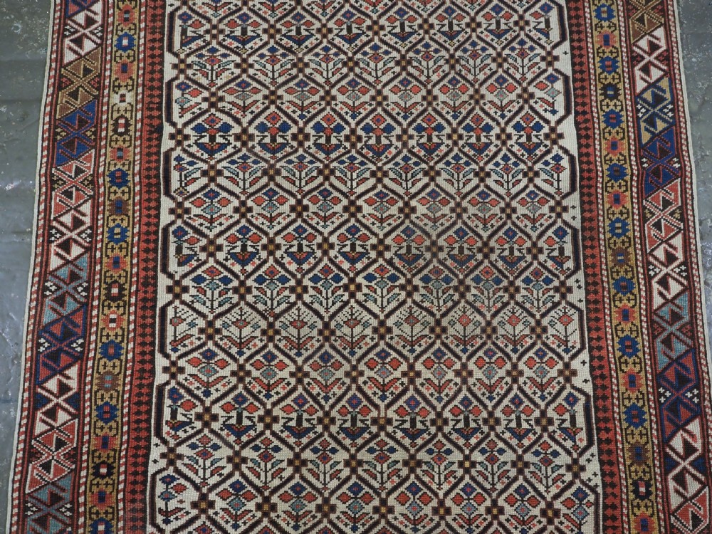 An antique Caucasian Shirvan wool prayer rug featuring an ivory field covered in a geometric floral lattice motif, enclosed by a multi-bordered frame and a stepped prayer arch at the top. View III