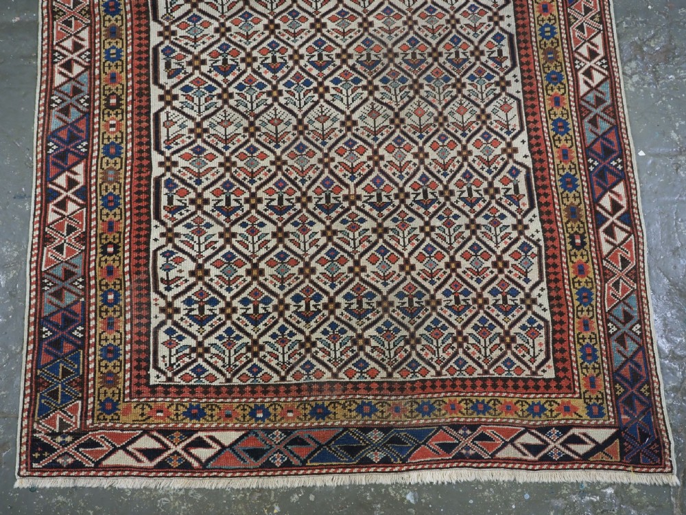 An antique Caucasian Shirvan wool prayer rug featuring an ivory field covered in a geometric floral lattice motif, enclosed by a multi-bordered frame and a stepped prayer arch at the top. View IV